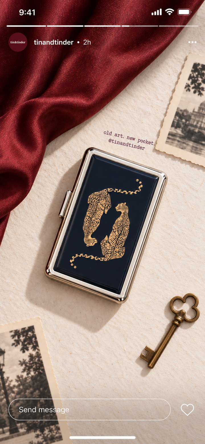 Navy tin card case with two gold leopards resting on a burgundy train seat by the window